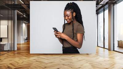 Happy young african woman casually dressed holding mobile phone standing isolated over gray background Wall mural